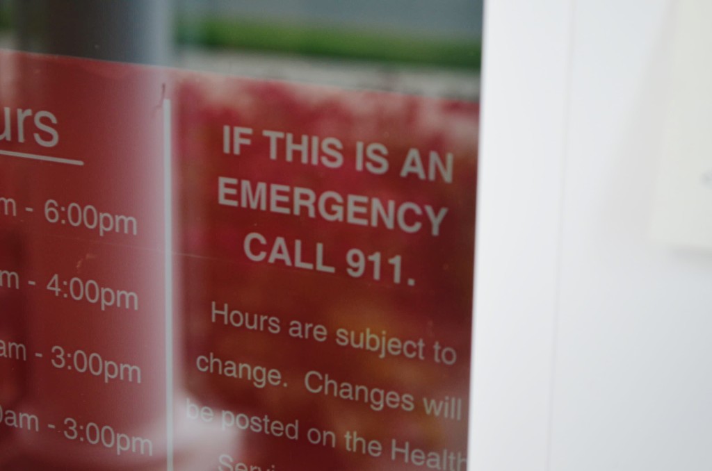 A sign on the Ellington Center’s main entrance. The text reads: “IF THIS IS AN EMERGENCY CALL 911. Hours are subject to change. Changes will be posted on the Health Services website.”